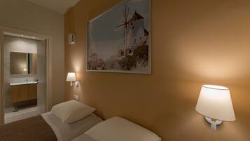 A hotel room with two beds, a bathroom with a sink, and a painting of a windmill on the wall.