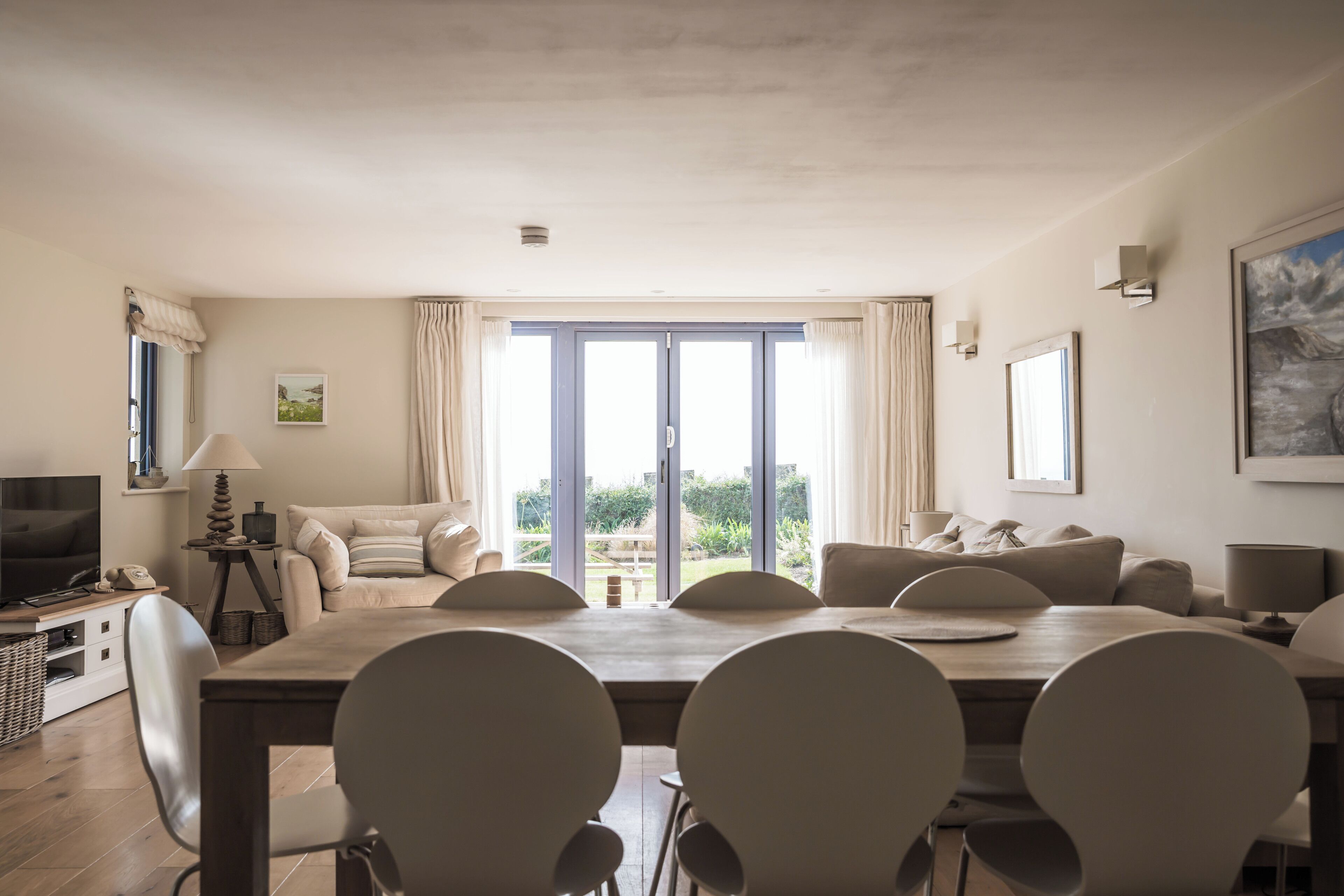 Un salón espacioso con una gran mesa de comedor de madera, varias sillas, un sofá y un televisor.