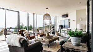 A spacious living room with a large window, a comfortable sofa, a coffee table, and a television. - Gara Rock (Salcombe)