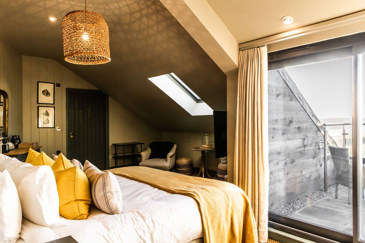 A hotel room with a bed, a hanging light fixture, a skylight, a view of the outside, and a balcony.