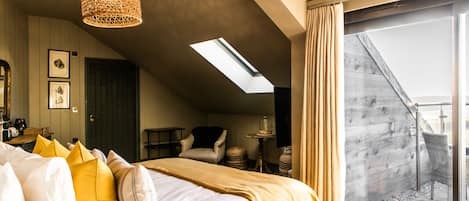 A hotel room with a bed, a hanging light fixture, a skylight, a view of the outside, and a balcony.