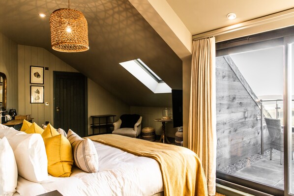 Habitación de hotel con cama, lámpara colgante, tragaluz, vista al exterior y balcón.