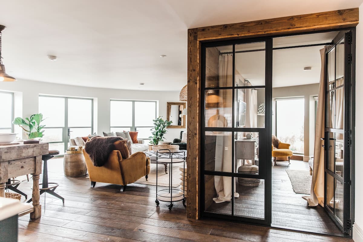 A spacious living room with wooden flooring, a yellow armchair, and a large sliding glass door leading to another room.