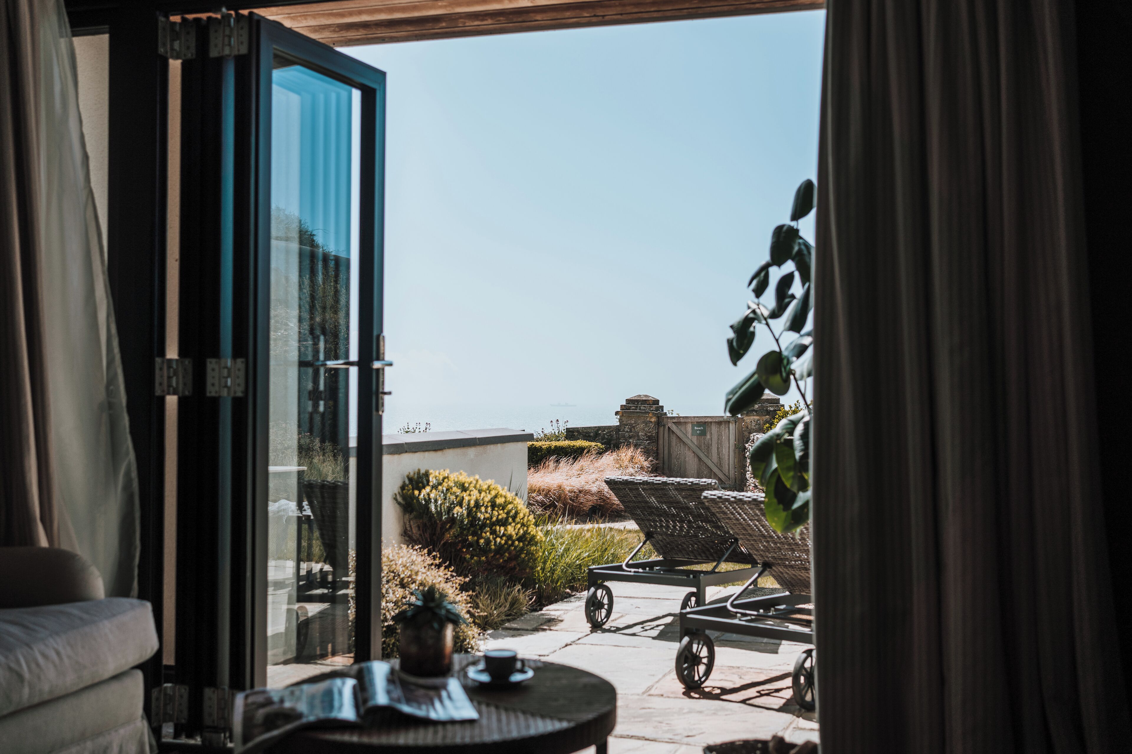 A room with a sliding glass door leading to a patio area with a chair, a table, and a potted plant.