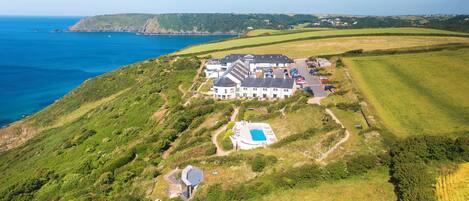 An aerial view of a coastal property with a large house, a swimming pool, and a parking area.