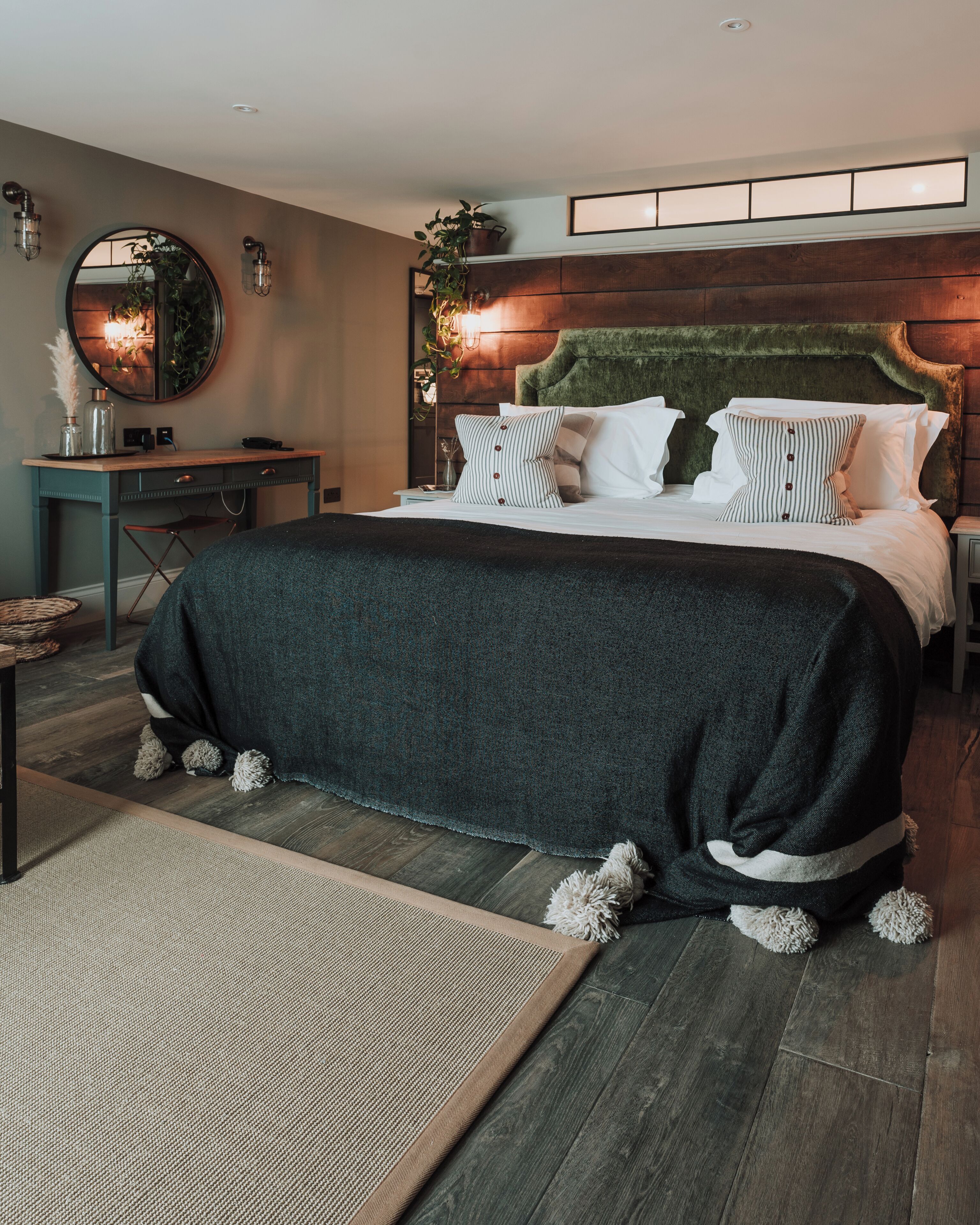 A modern bedroom with a large bed, a desk, and a mirror.