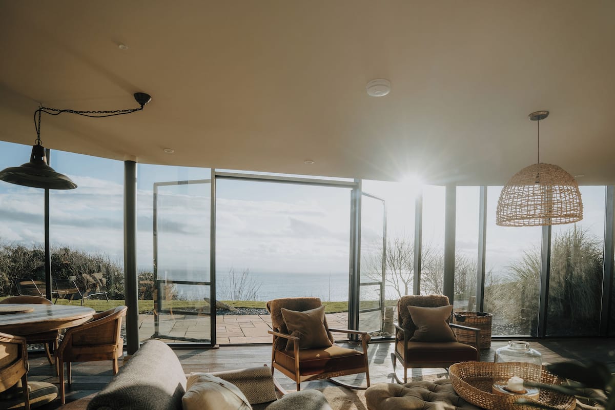 A spacious living area with a large glass door leading to an outdoor patio, furnished with wooden chairs and a round table.