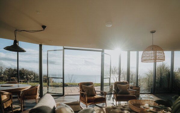 Amplia sala de estar con un gran ventanal que da a un patio exterior, amueblada con sillas de madera y una mesa redonda.