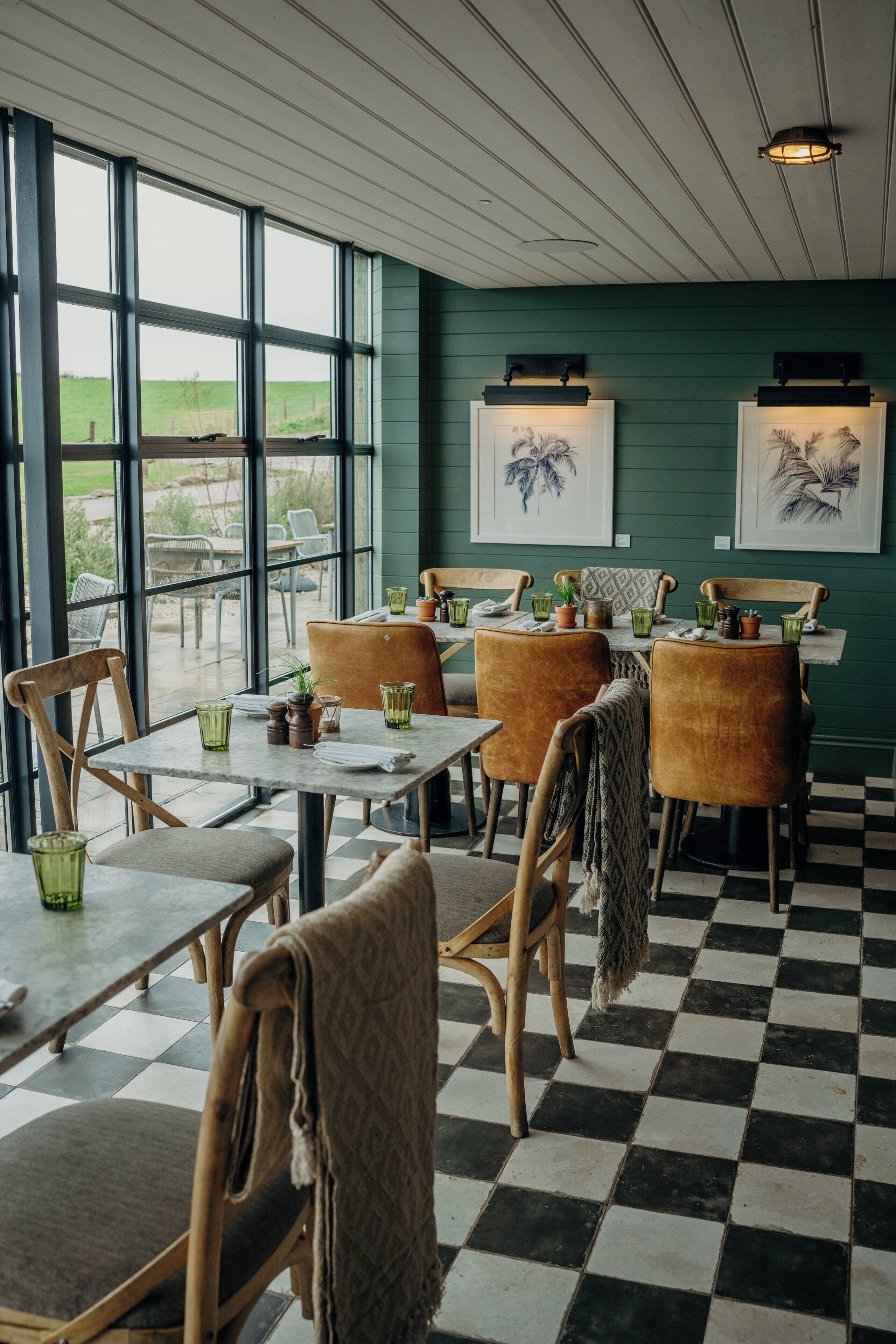 Ein Restaurant mit Schachbrettfußboden, Holztischen und -stühlen sowie grünen Gläsern.