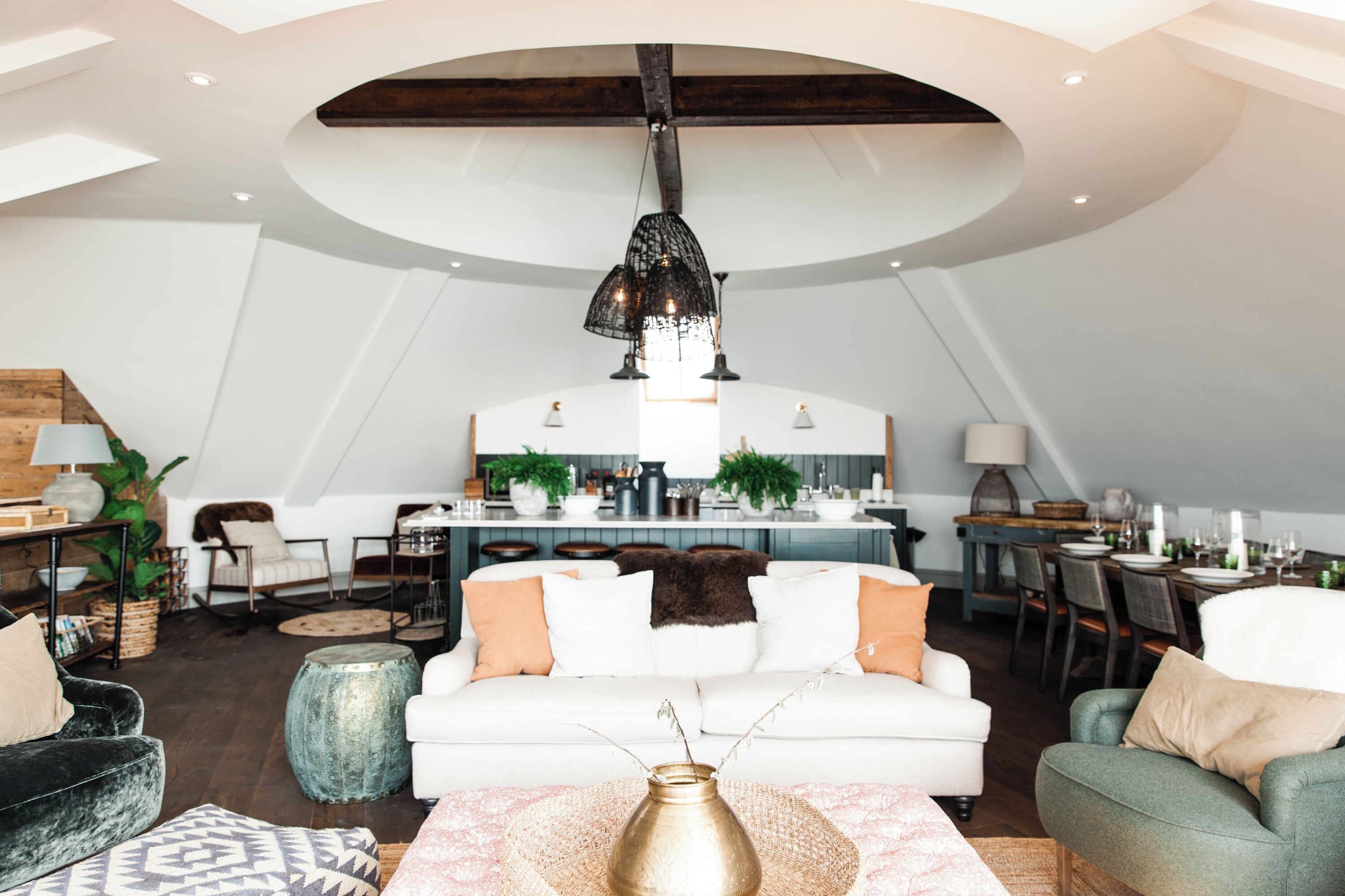 Un loft amplio con techo alto, un área de comedor central y una zona de estar acogedora con un sofá blanco y varias sillas.