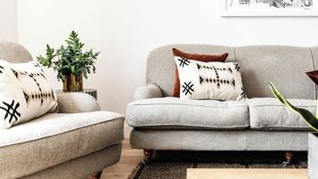 A living room with two grey sofas, one with a patterned pillow and the other with a plain pillow. There is a green plant in a vase on the floor.