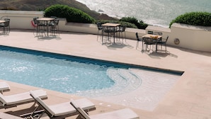 A poolside area with lounge chairs and tables, overlooking a body of water and a hilly landscape. - Gara Rock (Salcombe)