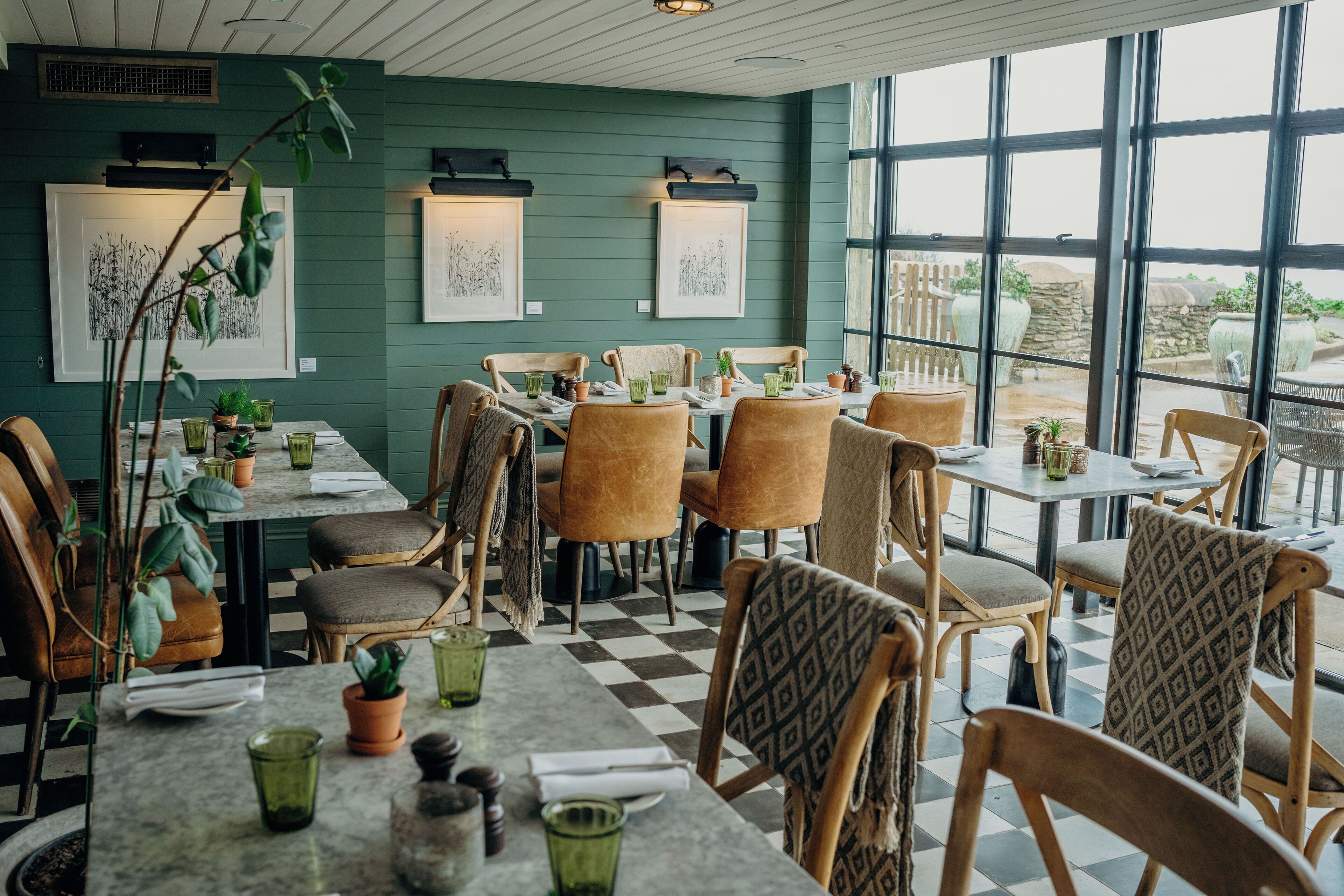 A restaurant with wooden chairs and tables, green walls, and artwork.