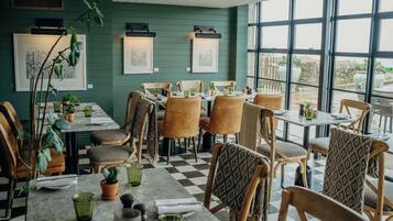A restaurant with wooden chairs and tables, green walls, and artwork.