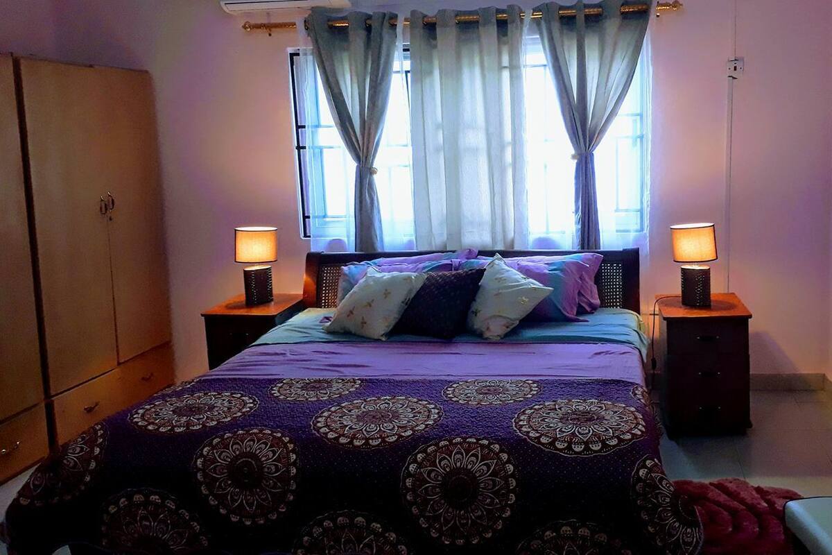 A bedroom with a bed, two bedside lamps, a window with curtains, and a wardrobe.