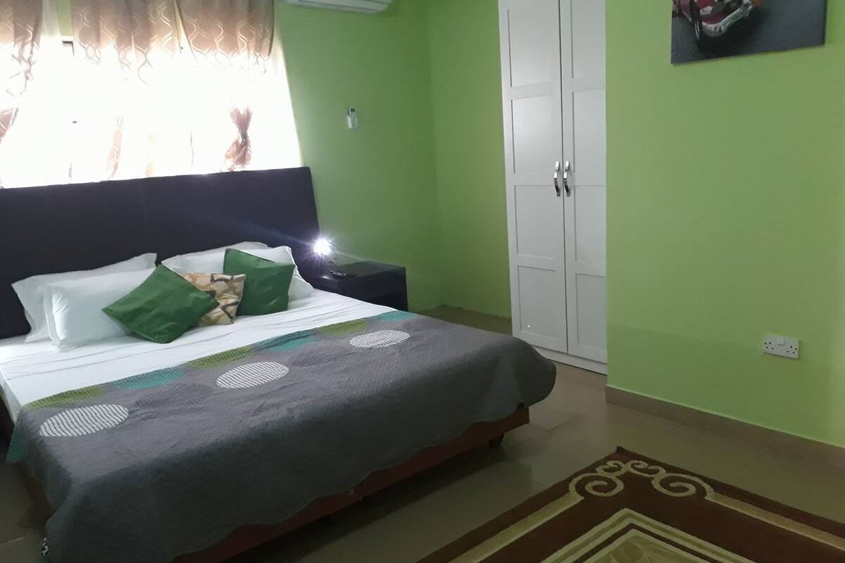 A bedroom with a bed, green walls, a white wardrobe, and a nightstand.