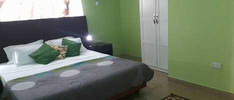 A bedroom with a bed, green walls, a white wardrobe, and a nightstand.