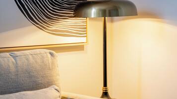 Une lampe moderne avec un abat-jour métallique, un élément décoratif mural texturé et un canapé de couleur claire.