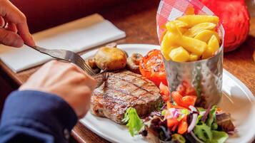 A plate with grilled steak, roasted potatoes, grilled tomatoes, a salad, and a cup of mango chunks.