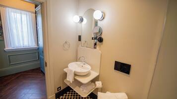 A bathroom with a white sink, mirror, and lights; a checkered floor; and a door leading to another room.