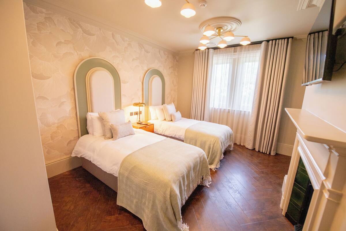 Ein Hotelzimmer mit zwei Betten, einem Kamin und einem großen Fenster mit Vorhängen.