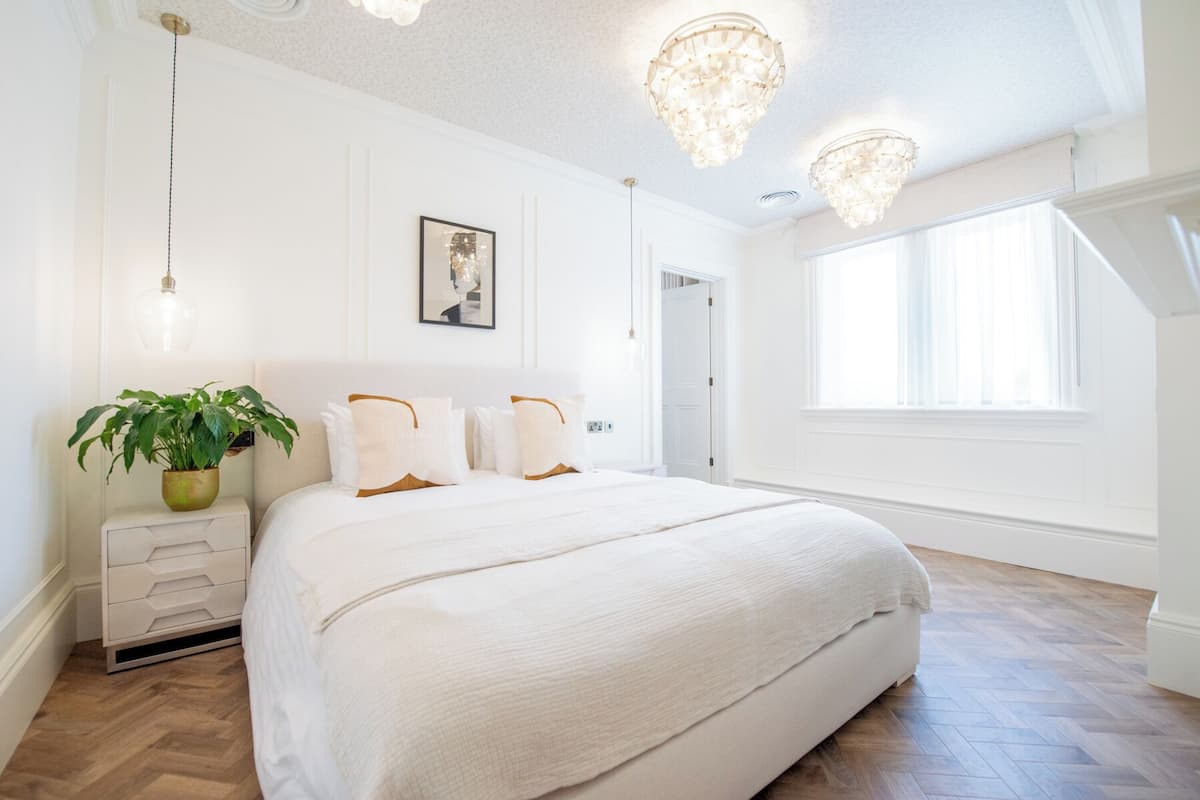 Ein Schlafzimmer mit einem großen Bett, einer Topfpflanze, einem gerahmten Bild an der Wand und einer Chandelier.