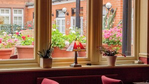 Una ventana con plantas en macetas y una lámpara, con vistas a un edificio de ladrillo y un jardín.