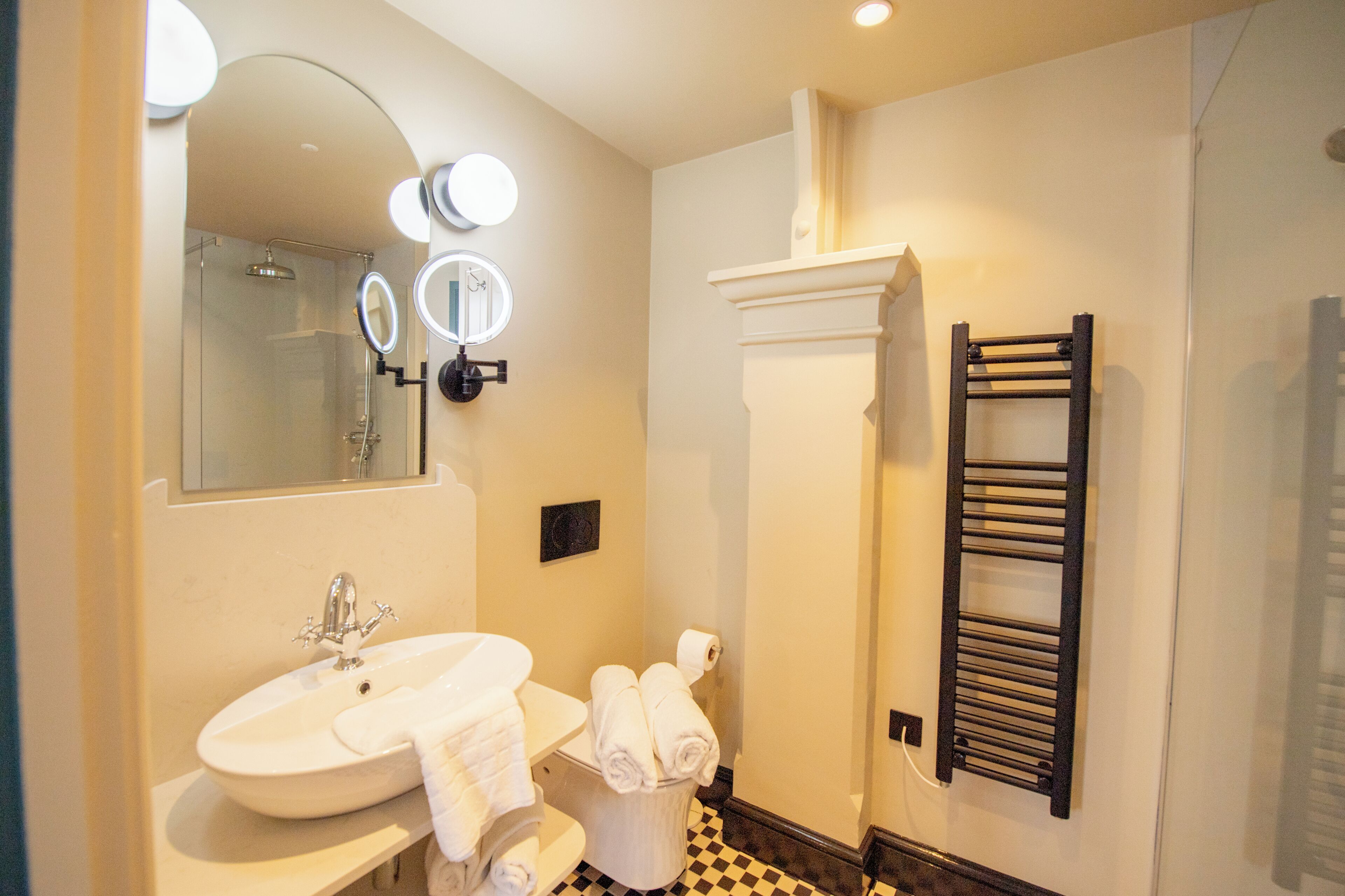 A bathroom with a sink, mirror, towel rack, and a shower.