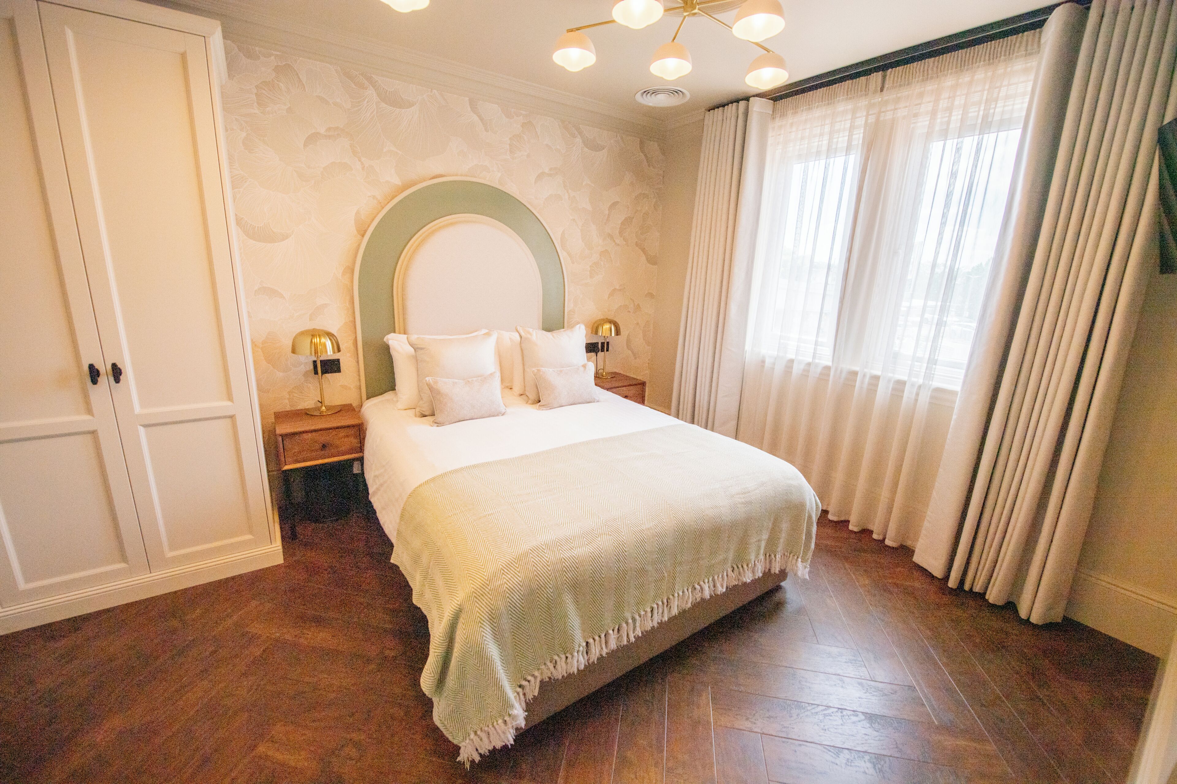 Un dormitorio con cama, mesitas de noche, un espejo y una ventana con cortinas.