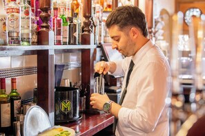 A bartender preparing a drink at a bar with shelves of liquor bottles. - The Carre Arms Hotel (Sleaford)