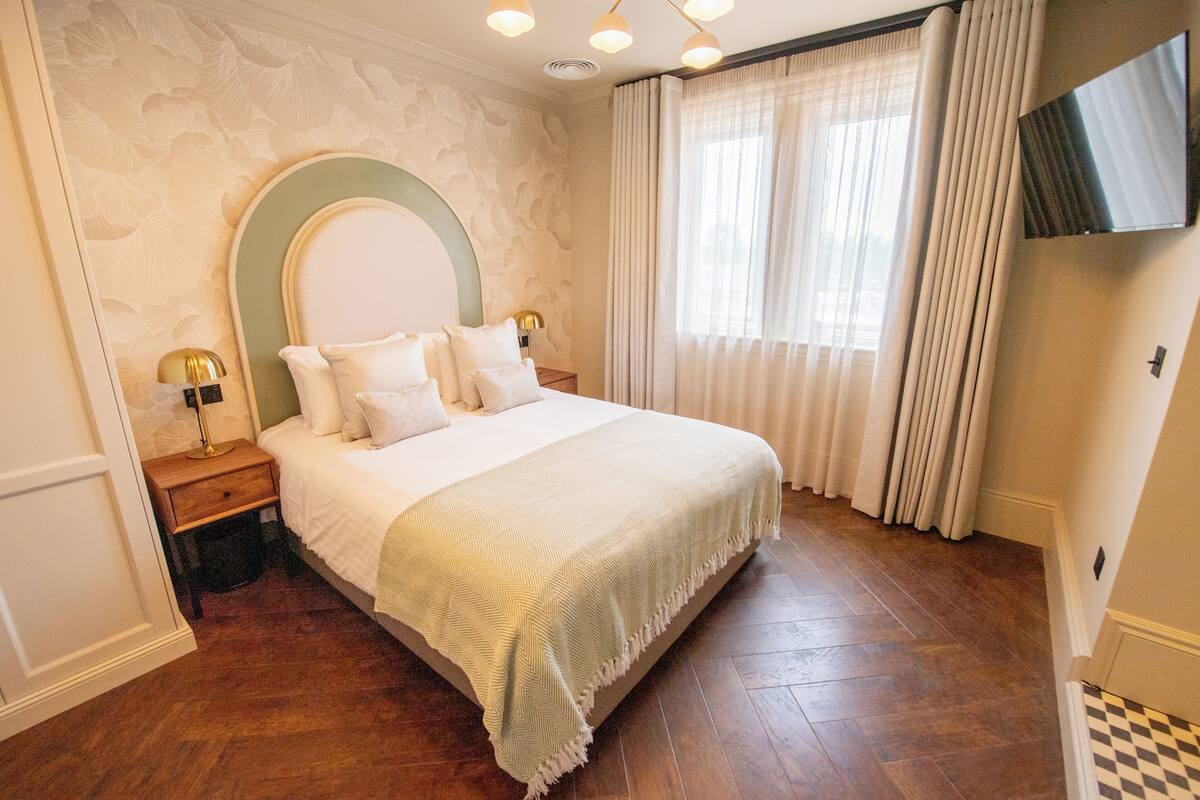 Ein Hotelzimmer mit Bett, Nachttisch, Fernseher und einem Fenster mit Vorhängen.