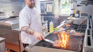 Un cocinero asando carne en una parrilla industrial en una cocina.