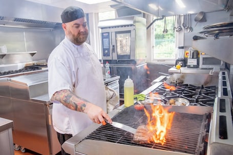 A chef grilling meat on a commercial grill in a kitchen.. The Carre Arms Hotel