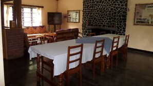 A dining area with a long table, wooden chairs, a stone wall, and a television.