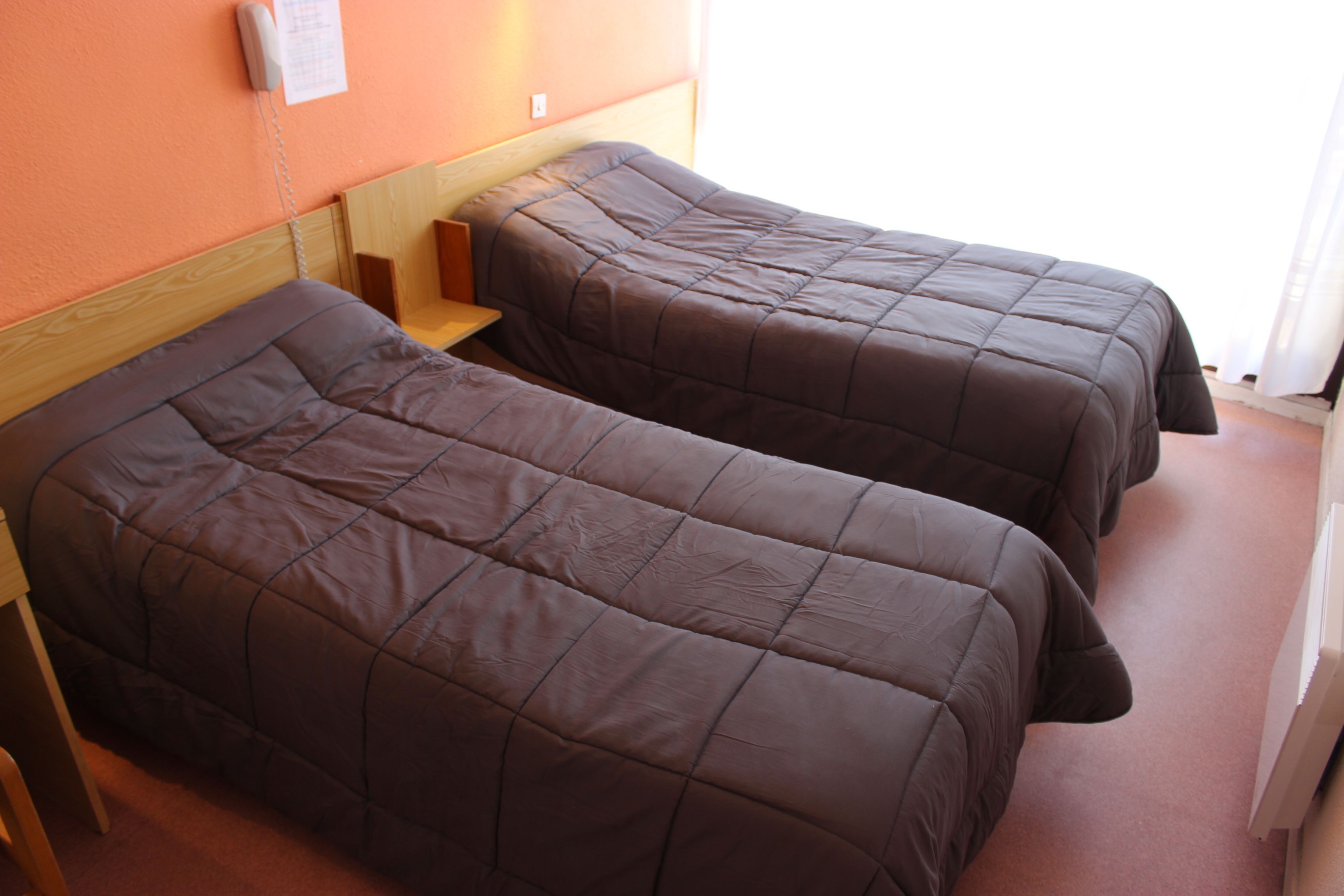 Two single beds with wooden headboards in a room with an orange wall and a white radiator.