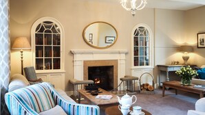 Uma sala de estar aconchegante com lareira, poltronas listradas, uma mesa de centro com um bule e uma estante de livros.