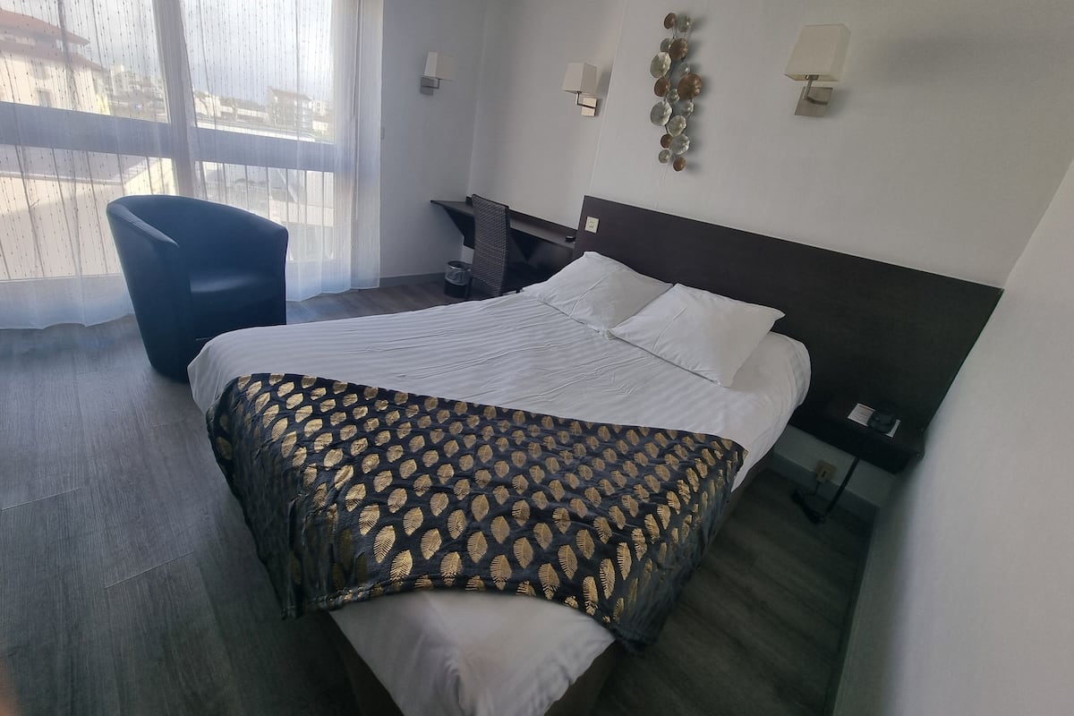 A hotel room with a bed, a chair, a desk, and a window with curtains.