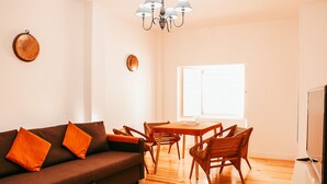 Una sala de estar con un sofá, sillas de madera, una mesa de comedor y un televisor.