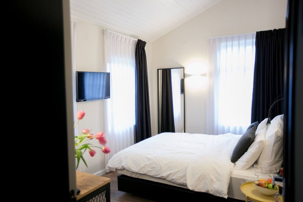 A hotel room with a bed, a TV mounted on the wall, a mirror, and a small table with a bowl of fruit.