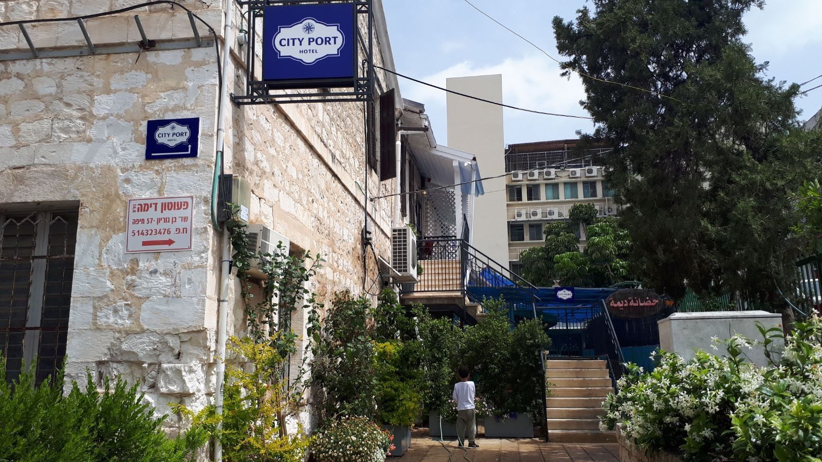 A stone building with a 'City Port Hotel' sign, a staircase, and a person walking.