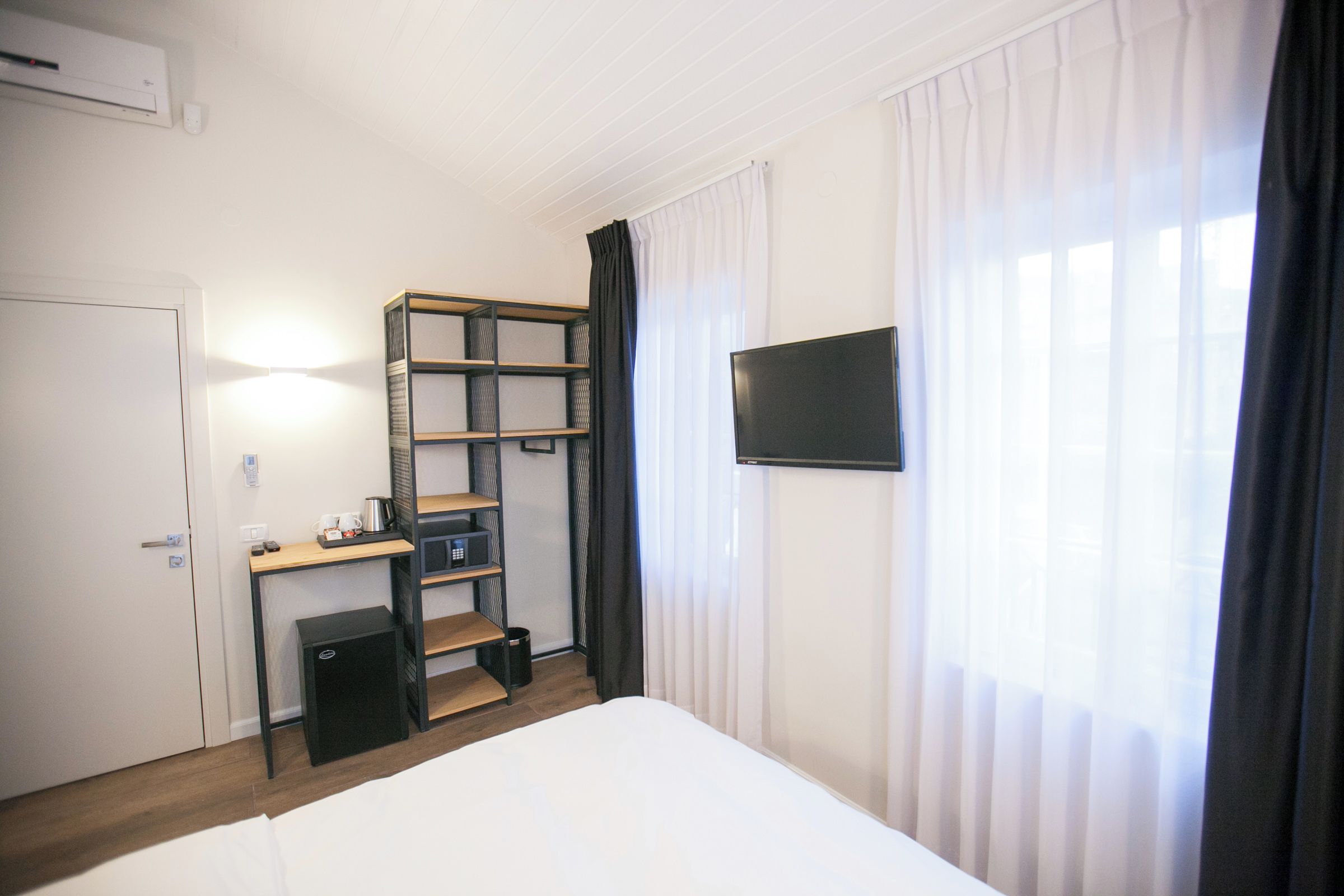 A hotel room with a bed, a desk with a computer, a TV, and a window with curtains.