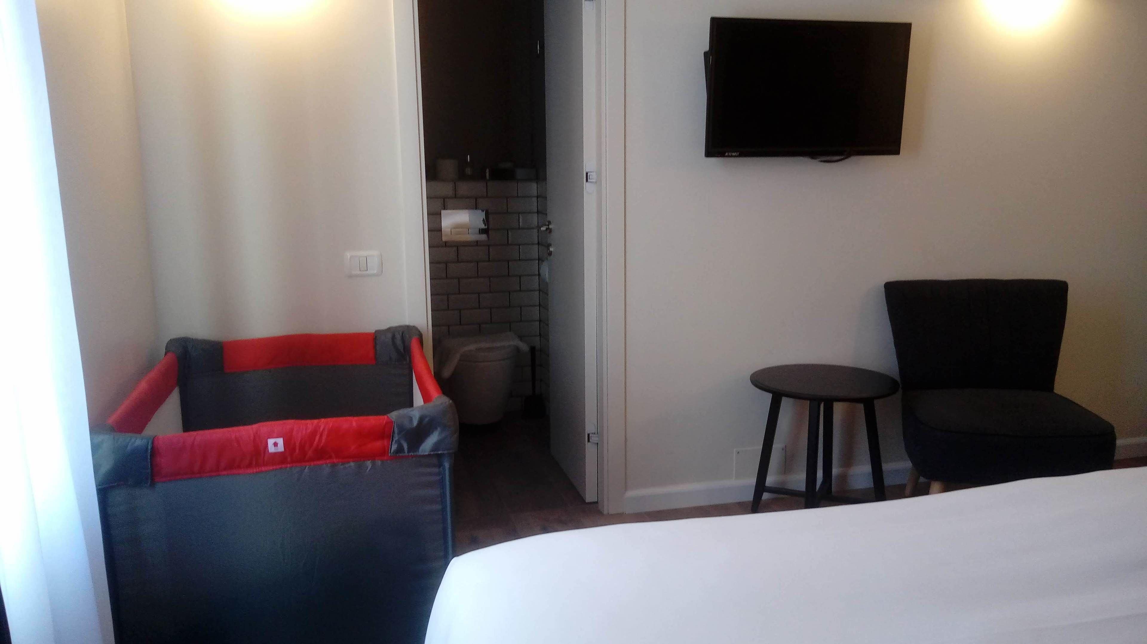 A hotel room with a bed, a TV mounted on the wall, a small table, and a chair.
