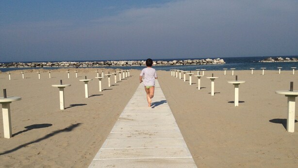 A concrete pathway leading to a beach with white posts on either side. - Hotel Lazzarini (Bellaria-Igea Marina)