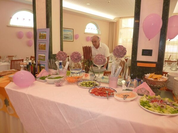 A buffet table with various food items and pink balloons.
