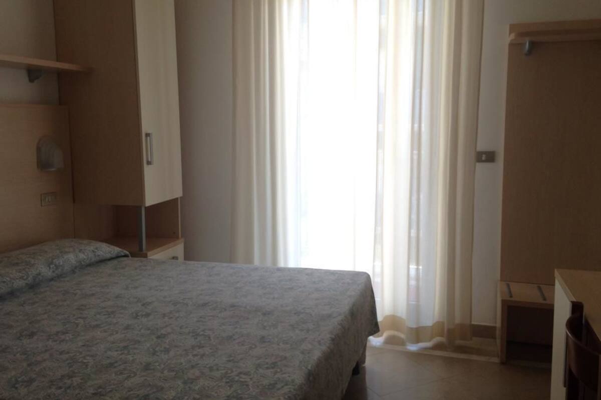 Ein Schlafzimmer mit einem Bett, einem Kleiderschrank und einem Fenster mit Vorhängen.