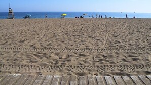 Une plage de sable avec une promenade en bois, un poste de surveillance pour les sauveteurs et des parasols de plage.