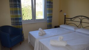 Ein Zimmer mit zwei Betten, einem blauen Stuhl und einem Fenster mit Vorhängen.