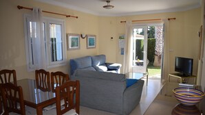 Ein Wohnzimmer mit einer Couch, einem Esstisch mit Stühlen, einem Fernseher und einem großen Fenster.