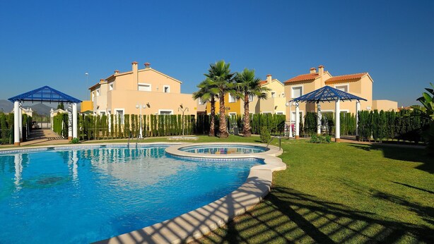 Ein Pool mit Sonnendeck, Palmen und einem Gebäude mit beiger Fassade.