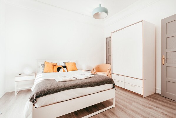 A modern bedroom with a bed, a wardrobe, a nightstand, and a hanging light fixture.